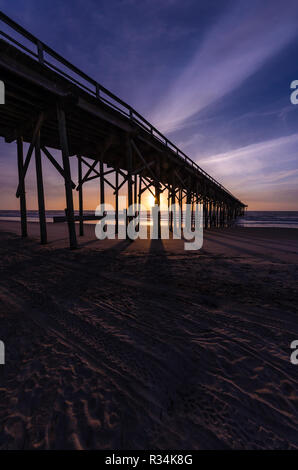 I raggi di luce durante il sunrise dietro un molo lungo la spiaggia Foto Stock