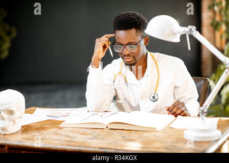 Ritratto di un giovane africano di etnia medico o studente di medicina in uniforme durante il lavoro o lo studio in ufficio o a scuola Foto Stock