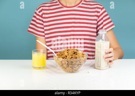 Sana colazione con cereali integrali, latte e succo di frutta. Illustrativi immagine minimalista di cibo vegetariano sul tavolo e affamati e persona Foto Stock