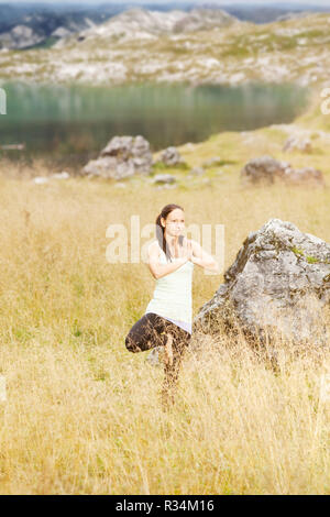 Lo yoga pone nell'erba alta nella parte anteriore di un lago di montagna nelle Alpi Foto Stock