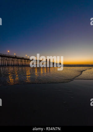 Un molo riflettendo sulla superficie dell'oceano mentre il sole tramonta in Oceanside, California, Stati Uniti d'America Foto Stock