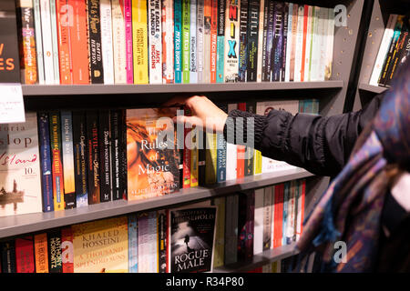 Una donna che seleziona e raccoglie un libro di libro cartaceo da una libreria in una libreria Waterstones, Regno Unito Foto Stock