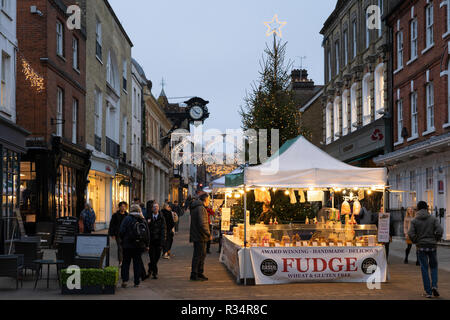 Shoppers guardando una farsa stallo in Winchester High Street con un albero di Natale e le luci in background Foto Stock