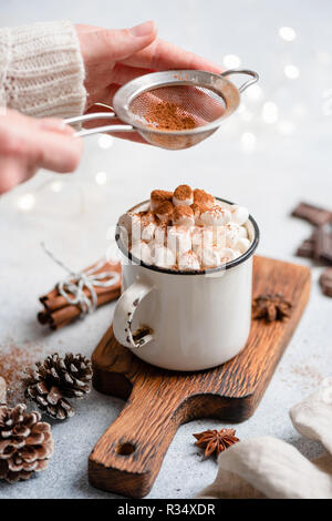 Cioccolata calda con marshmallows in tazza. Setacciatura di cacao in polvere sul cioccolato caldo a bere con marshmallow Foto Stock