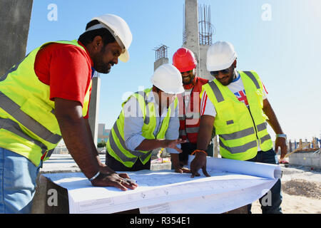 Gli uomini con il blueprint in mano lavorano nel settore della costruzione e indossare elmetto e giubbotto di sicurezza, essi stare insieme sotto il cielo blu e s Foto Stock