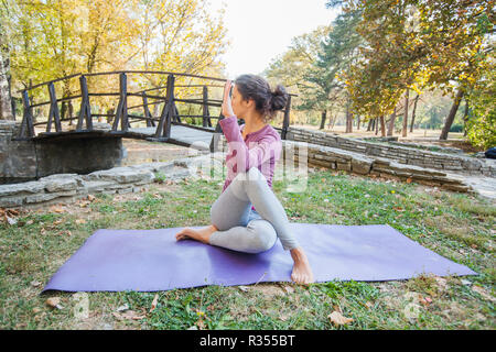 Sporty giovane donna facendo esercizio di Yoga, Ardha Matsyendrasana, seduto Mezza torsione spinale, metà signore dei pesci pongono, nel parco. Foto Stock