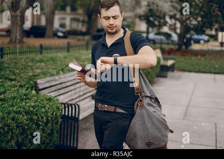 Bel giovane uomo è in viaggio con un notebook e un sacchetto in città Foto Stock