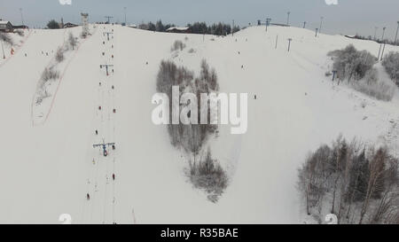 Vista aerea: gli sciatori e gli snowboarder andando giù il pendio nel giorno d'inverno. Gli sciatori e gli snowboarder godendo su pendii di ski resort nella stagione invernale. Foto Stock