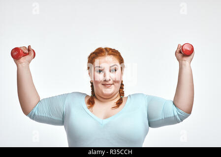 Divertente dai capelli rossi, chubby donna è sorridente e holding manubri Foto Stock