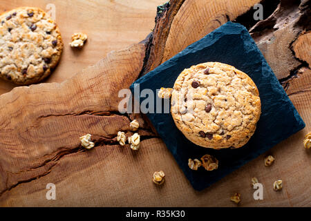 Concetto di cibo organico artigianale cioccolato cookie su pietra ardesia su piastra in legno rustico sfondo con spazio di copia Foto Stock