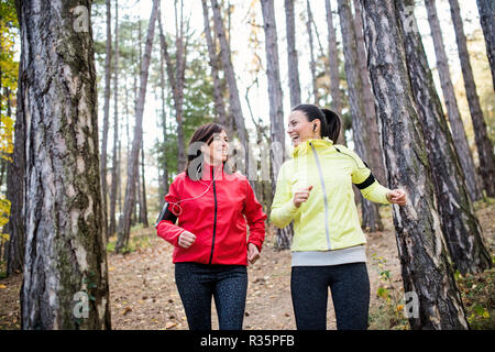 Femminile con gli auricolari e smartphone jogging all'aperto nella foresta. Foto Stock