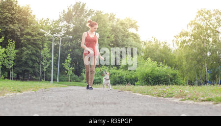 Una ragazza con un cane al guinzaglio del Jack Jack Russell Terrier passeggiate lungo il vicolo nel parco Foto Stock