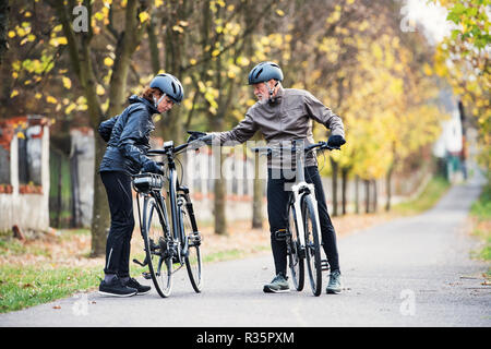 Attivo coppia senior con electrobikes in piedi all'aperto su una strada in natura. Foto Stock