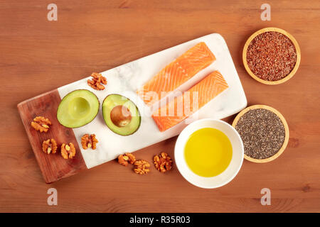 Una sana omega 3 la dieta alimentare. Salmone crudo, avocado, noci, semi di Chia e flaxseeds, girato da sopra al buio su un rustico sfondo di legno con spazio di copia Foto Stock