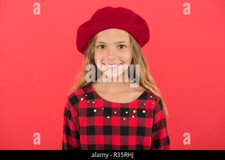 Kid poco carino ragazza sorridente in posa di hat sfondo rosso. Moda beret accessorio per la femmina. Come indossare il francese beret. Beret style ispirazione. Come indossare beret come moda ragazza. Foto Stock