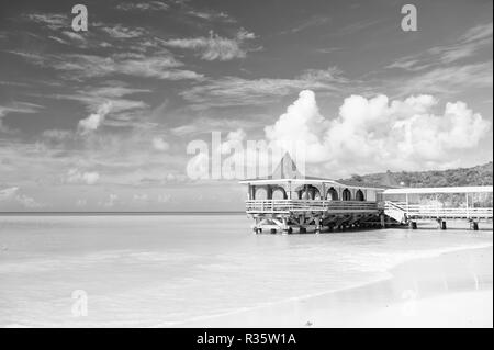 Venite a soggiornare. Turchese del mare calmo e bungalow terrazza sull'acqua. Vacanza mare spiaggia di sabbia accogliente casa tropicale bungalow.st Johns Antigua. Idilliaco giorno di sole in riva al mare a cielo blu. Paradise resort sul mare. Foto Stock