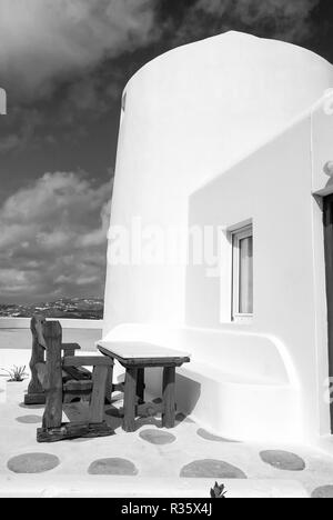 Tavolo e panca in cantiere di Mykonos, Grecia. Casa sul paesaggio di montagna, architettura. Edificio con pareti dipinte di bianco sul cielo blu. Vacanze estive sull'isola del Mediterraneo. Viaggi e concetto di viaggio. Foto Stock