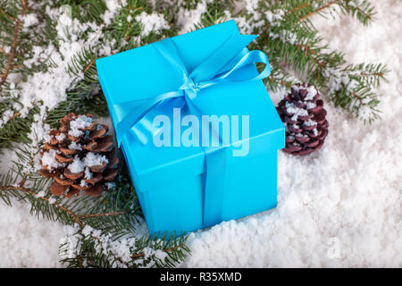 Blu regalo di Natale scatola con pigne e albero sempreverde rami su una superficie della neve Foto Stock