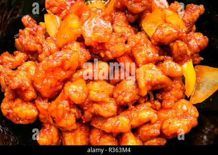 La cucina cinese è piatto - vista superiore di fritto di pollo a pezzi con ananas e il peperone e la cipolla (dolce e aspro di pollo) nel vaso nero close up Foto Stock