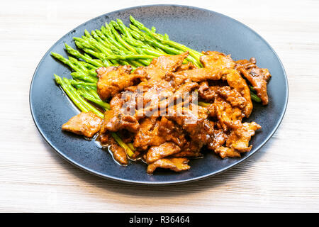 La cucina cinese è piatto - Carni bovine fritti in salsa di soia con asparagi cotti sulla piastra nero su grigio pannello di legno Foto Stock