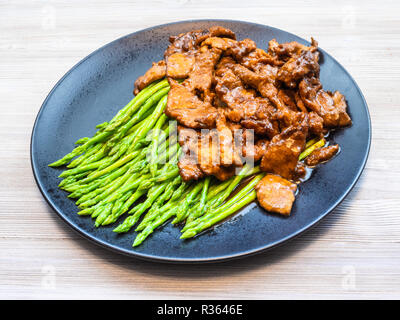 La cucina cinese è piatto - Carni bovine fritti in salsa di soia con asparagi cotti sulla piastra nera sulla tabella grigia Foto Stock
