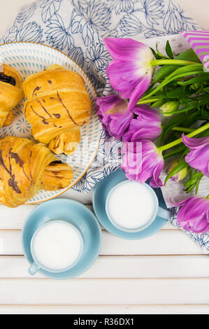 Tre croissant, due tazze di caffè sul tavolo e un mazzo di bellissimi tulipani-close-up. Foto Stock