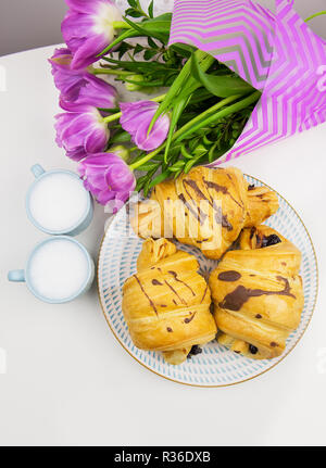 Tre croissant, due tazze di caffè sul tavolo e un mazzo di bellissimi tulipani. Foto Stock