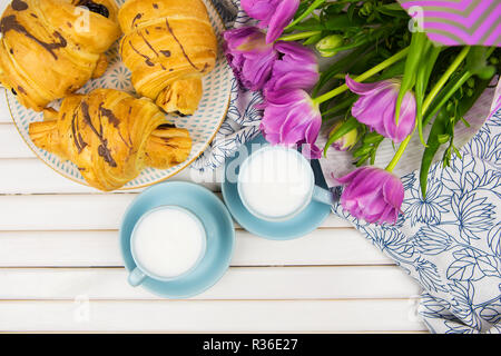 Tre croissant, due tazze di caffè sul tavolo e un mazzo di bellissimi tulipani-close-up. Foto Stock