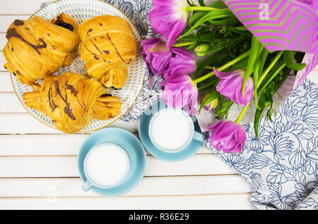 Tre croissant, due tazze di caffè sul tavolo e un mazzo di bellissimi tulipani-close-up. Foto Stock