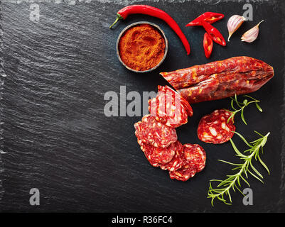 Il salame chorizo tagliato a fettine su un nero ardesia piastra con paprika affumicata affettata, peperoncino e rosmarino fresco, vista da sopra, close-up, flatlay, copia sp Foto Stock