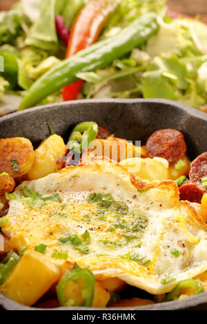 Uovo fritto e patate al forno con salsiccia chorizo e peperoncini verdi in padella Foto Stock