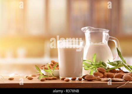 Alternativa latte di mandorle in un bicchiere e caraffa di vetro su di un tavolo di legno in una cucina rustica. Vista frontale. Composizione orizzontale. Foto Stock