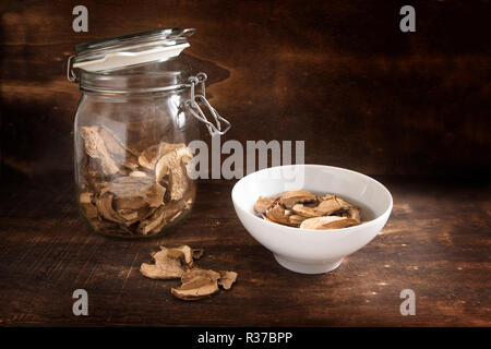 Funghi porcini essiccati in un vasetto di vetro e imbevuti di acqua come preparazione per la cottura su scuro legno rustico con spazio di copia selezionato, focus, strette dept Foto Stock