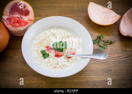 Dolce di farina di avena con fette di pompelmo rosso in un vaso in ceramica isolata sul tavolo di legno Foto Stock