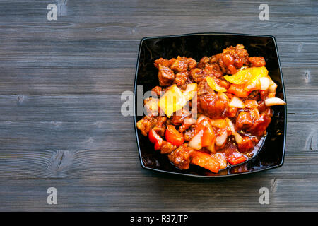 La cucina cinese è piatto - vista superiore del recipiente nero con pezzi di carne di maiale fritto in salsa con ananas, il peperone e la cipolla (carne di maiale in salsa agrodolce) Foto Stock