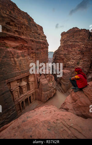 Bedouin si siede sul bordo di una roccia e si guarda dal di sopra nella gola Siq, faraone treasure house scolpito nella roccia, Foto Stock