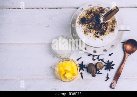 Bulletproof caffè. Dieta Ketogenic caffè con olio di noce di cocco e il burro di ghee). Tazza di caffè antiproiettile e ingredienti, paleo dieta. Sul legno bianco b Foto Stock