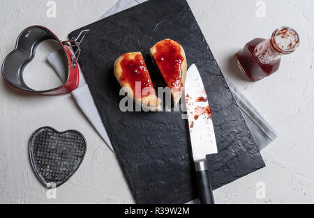 Gustosi piatti fatti in casa a forma di cuore torta al lampone affettato in due su un tagliere. Salsa di fragole versato sopra la torta. Direttamente sopra il punto di vista con il kitch Foto Stock