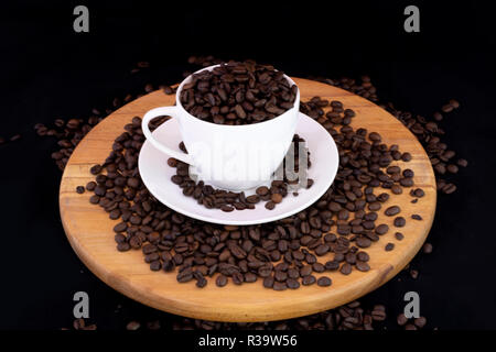 I chicchi di caffè all'interno della tazza da caffè in legno con isolati su sfondo nero Foto Stock