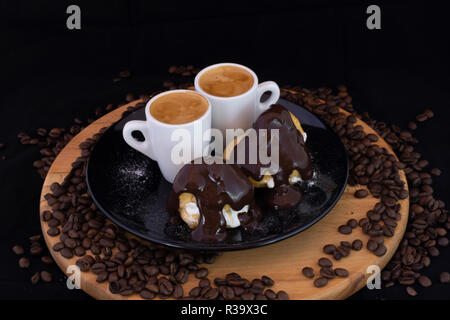 Profiterols ed espresso su legno isolato con sfondo nero Foto Stock