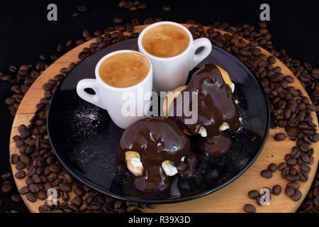 Profiterols ed espresso su legno isolato con sfondo nero Foto Stock