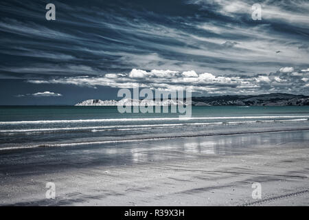 Bellissimo paesaggio marino con spiaggia di sabbia bianca e blu le onde del mare e le montagne e il cielo nuvoloso per lo sfondo, Nuova Zelanda Foto Stock