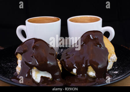 Profiterols ed espresso su legno isolato con sfondo nero Foto Stock