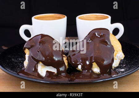 Profiterols ed espresso su legno isolato con sfondo nero Foto Stock