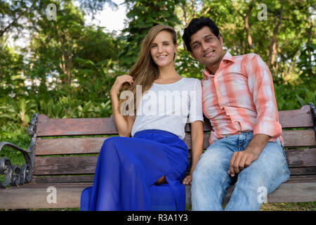 Felice multi etnico Coppia sorridente e seduta sul banco di legno in Foto Stock