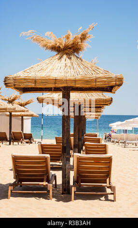 La paglia di ombrelloni e sedie a sdraio su una bellissima spiaggia Foto Stock