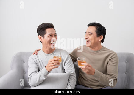 Maschio asiatici amici e seduto sul divano e di bere whisky, discutendo di qualcosa e ridere Foto Stock