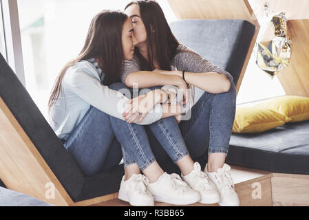 Due figlie gemelle sedersi in una poltrona a tenuta per loro nella zona di ricreazione. Sorelle in posa e divertimento trascorrere del tempo. Sempre unire l amicizia e la gioventù concept Foto Stock