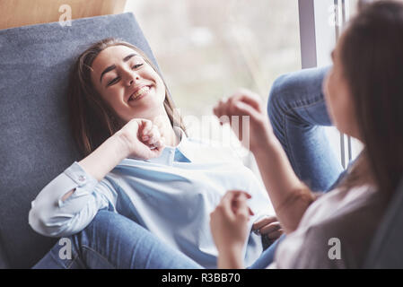 Due figlie gemelle sedersi in una poltrona a tenuta per loro nella zona di ricreazione. Sorelle in posa e divertimento trascorrere del tempo. Sempre unire l amicizia e la gioventù concept Foto Stock