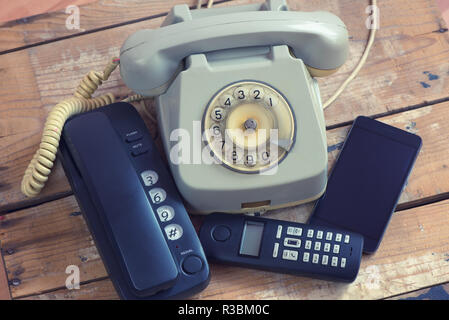 Tipi diversi di telefoni telefono fisso, smartphone, telefono con la manopola sul pannello di legno Foto Stock